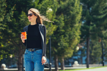 A beautiful girl walks down the street with coffee.