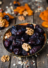 Dates and walnuts in vintage bowl on wooden background with dried apricot. Selective focus