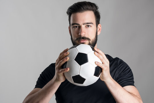 Friendly confident soccer player holding ball looking at camera over gray studio background. Horizontal orientation. - Powered by Adobe