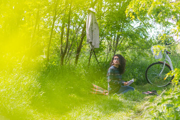 Lovely brunette teen with bicycle, reading a book in a park on a sunny day
