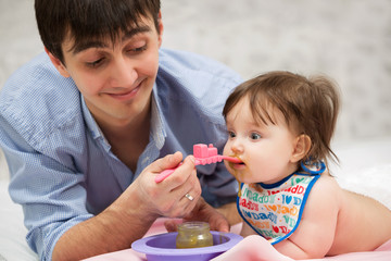 Father feeding baby girl on blanket at home