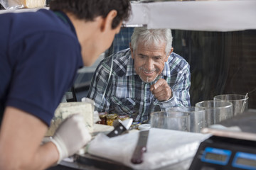 Obraz premium Man Selecting Cheese From Display Cabinet In Shop