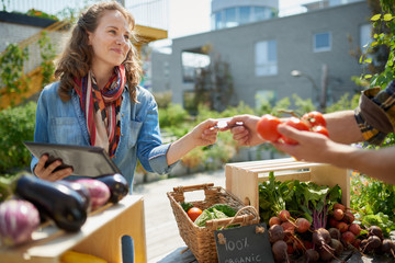 Friendly woman tending an organic vegetable stall at a farmer's market and selling fresh vegetables from the rooftop garden