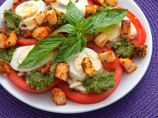 Healthy salad with tomatoes, boiled eggs, pesto and croutons. Close up horizontal shot. Cropped