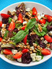 Fresh green salad with strawberries, blue cheese, walnuts, pecans and basil. Vertical shot, high angle view