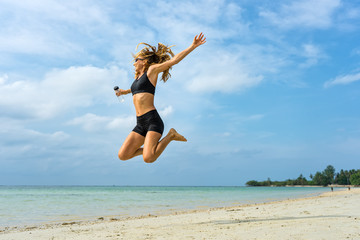 Young athletic woman jumping up on a tropical beach
