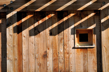 façade en bois avec petite fenêtre et ombre de poutres