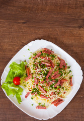 spaghetti pasta with salami sausage in a plate on wooden table