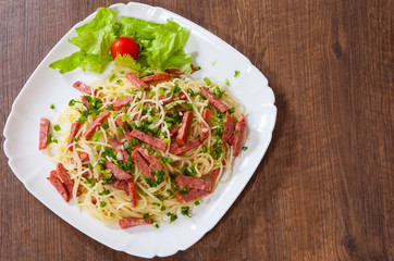 spaghetti pasta with salami sausage in a plate on wooden table
