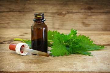 nettle tincture in a small bottle and fresh leaves on rustic wood