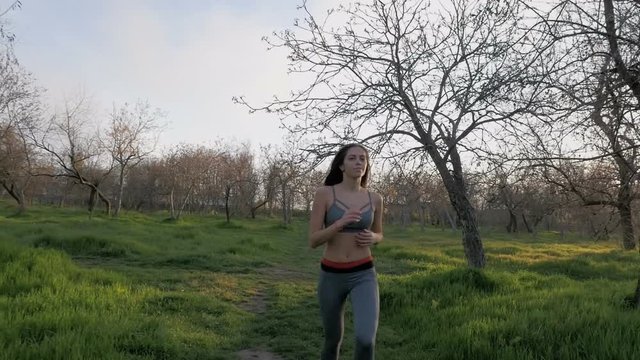 Young beautiful woman running in park at sunset, slow motion