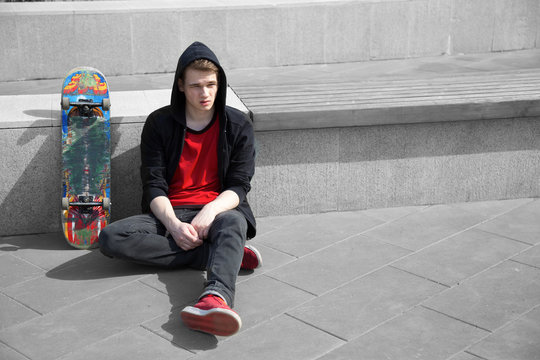 young skater resting on ground, skate board stands near