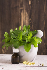 Mint sprigs, peppermint oil and pills over wooden table