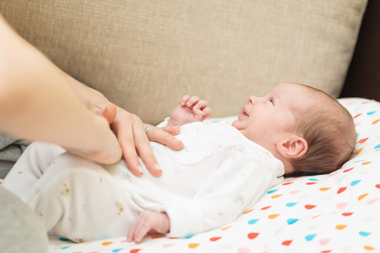 Newborn Colicky Baby Dressed In White Laying On Her Back, Mother's Hand On Her Tummy Helping Her With Colic