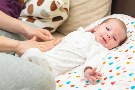 Newborn colicky baby dressed in white laying on her back, mother's hand on her tummy helping her with colic