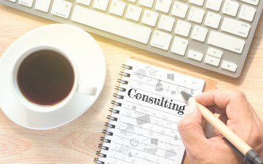 Hand writing on book message Consulting. A keyboard and a glass coffee table.Vintage tone.