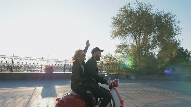 Happy young hipster couple riding a vintage scooter in city center and having fun, slow motion