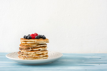 Pancakes with blueberries and raspberry on blue wood background 
