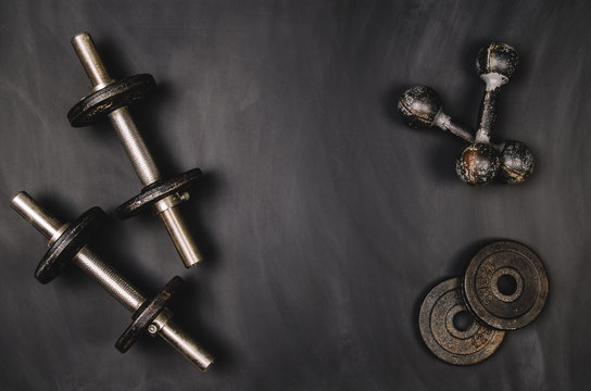 Iron dumbbells on a black chalkboard seen from above. Photo taken from above, top view. Conceptual image background for sport or fitness advertising. Horizontal image.
