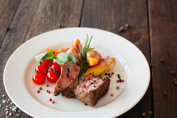 Medium rare pork steak with fresh vegetables on white plate. Top view food photography of pork steak with potatoes and tomatoes cherry. Prepared meat with vegetables on dark wooden background. 