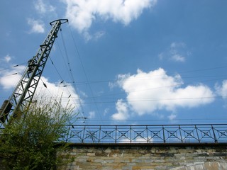 Eisenbahnbrücke mit Strommast und Geländer vor blauem Himmel mit weißen Wolken bei Sonnenschein in Bielefeld im Teutoburger Wald in Ostwestfalen-Lippe