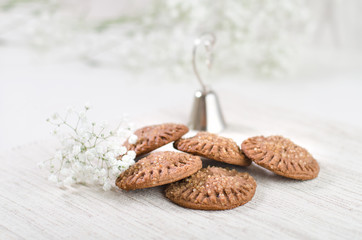 Chocolate cookies, white flowers and small bell on a light fabric