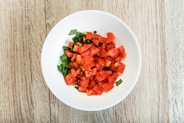 Sliced tomatoes and basil in a bowl on a wooden table