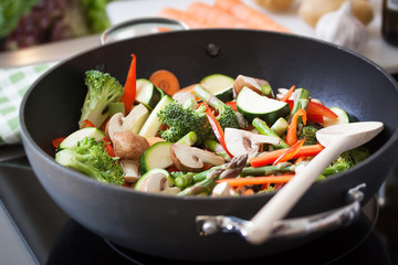 Wok stir fry vegetables with zucchini, spring asparagus, paprika, carrot and broccoli, closeup in a wok pan in a kitchen, selective focus