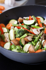 Wok stir fry vegetables with zucchini, spring asparagus, paprika, carrot and broccoli, closeup in a wok pan in a kitchen, selective focus