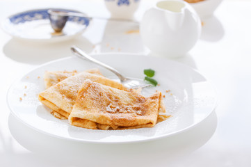 French crepes or pancakes with sugar powder, nuts and fresh mint on a white plate on a white background for breakfast, closeup