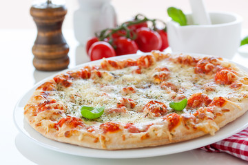 Fresh baked pizza with melted cheese, Italian herbs and tomato sauce and fresh basil on a white plate on a kitchen background, selective focus