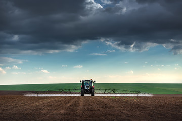 Obraz premium Farming tractor plowing and spraying on field