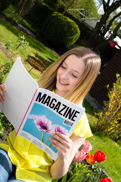 Junge Frau liest im Garten Zeitschrift