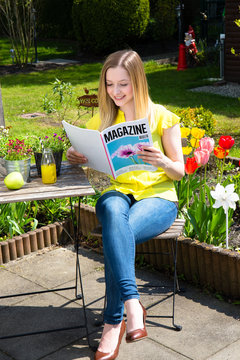 Junge Frau liest im Garten Zeitschrift