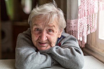 Portrait of an elderly woman, close-up, sitting at the table. - obrazy, fototapety, plakaty