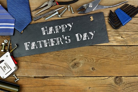 Happy Father's Day written on slate with corner border of tools on old wood background