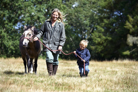 Mother and son walking pony in field