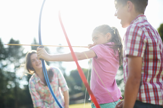 Girl learning archery from teenage sister and brother