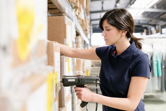 Female warehouse worker using barcode scanner on box in distribution warehouse