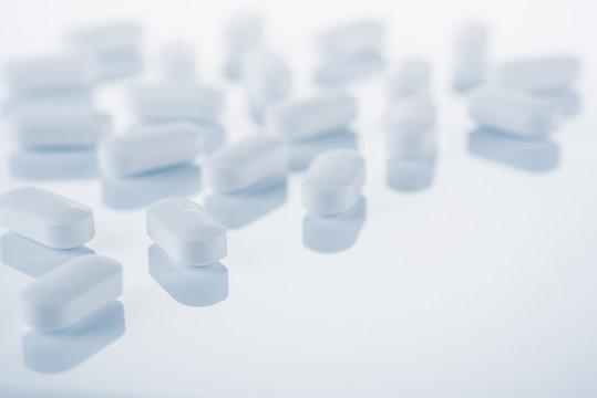 Medical concept or theme image with pills in the foreground. Product photo taken from above, low angle. Top view of medical pills on a glass, reflective table.