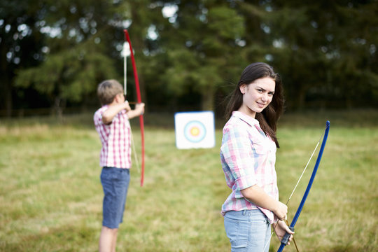 Portrait of teenage girl practicing archery with brother