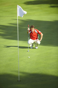 Front view of golfer crouching down in front of golf flag considering strategy
