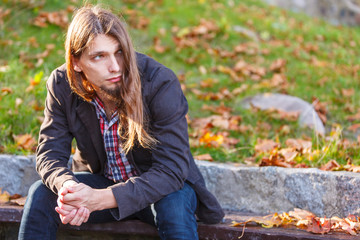 Man long hair sitting on bench in autumn park