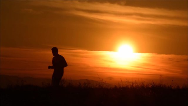 A man running on the background of an orange sunset sky, slow motion, silhouette.   Silhouette of man running against sunset, 
