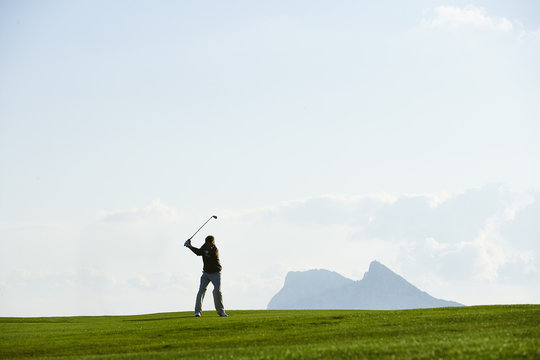 Golfer taking golf swing in front of mountain range