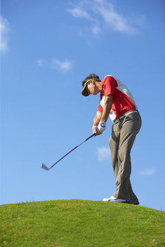 Low angle view of golfer on hill wearing sun visor holding golf club