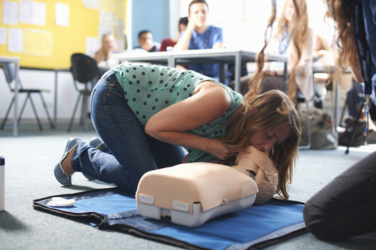 College student performing CPR on mannequin in class