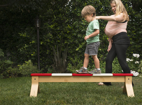Mother helping son walk across balance bar in garden