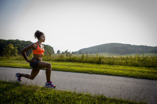 Young female runner stretching on rural park path