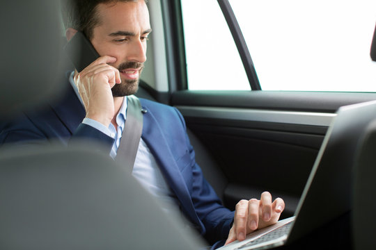 Young businessman chatting on smartphone in back seat of car